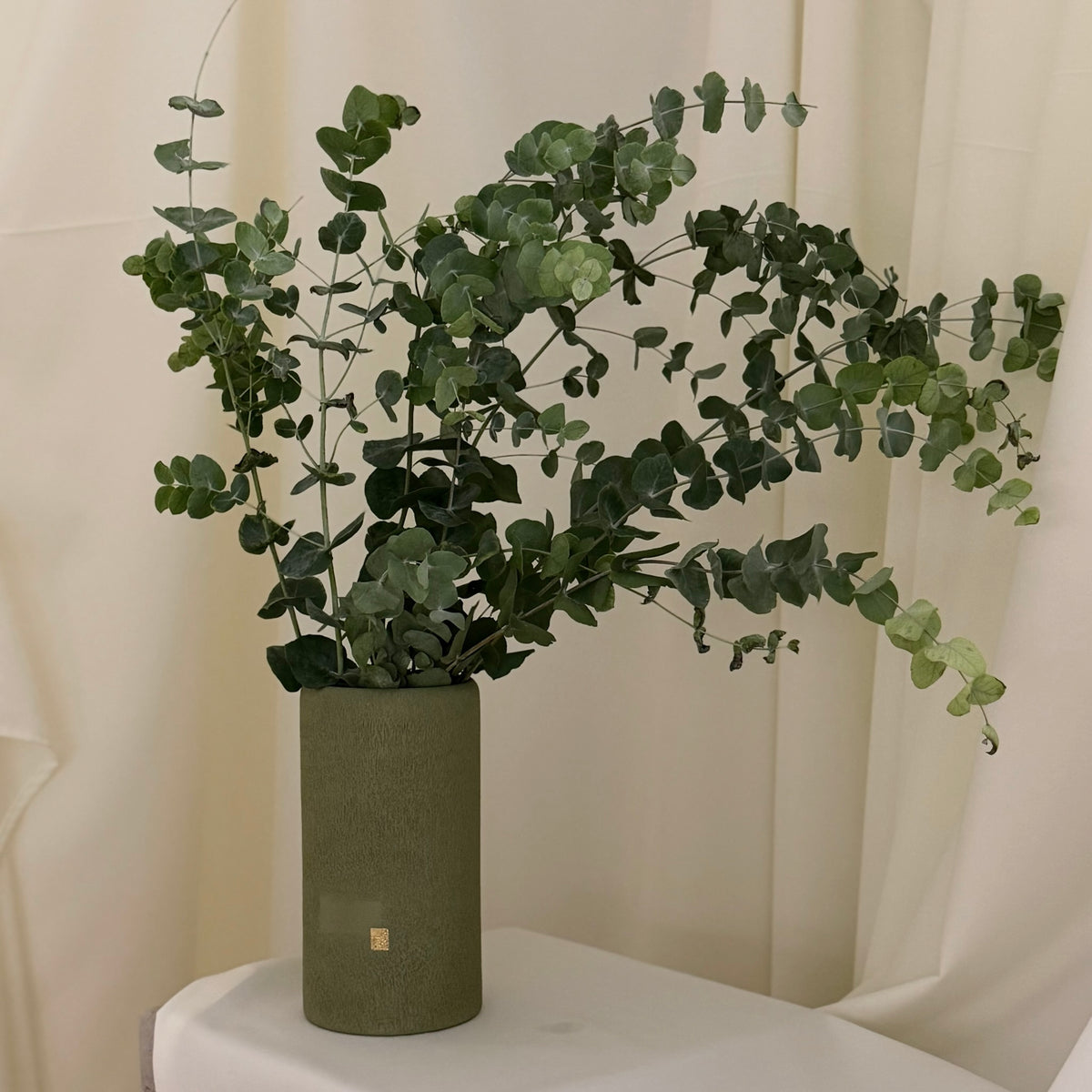 Jarrón Orah en porcelana verde oliva con ramas de eucalipto.